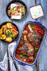 Traditional Greek roasted leg of lamb with feta and potatoes in tomato sauce offered as top view in a rustic skillet