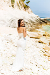 Fototapeta na wymiar Amazing girl in a white dress poses on the stones by the sea