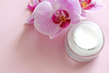 Skincare product for facial with pink orchid decoration on the pink background. White beauty cream top view.