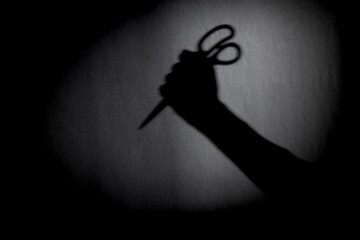 man with scissors silhouette over dark wall. black and white photo can be used for illustrating horror and violence attack. crime concept. simple. selective focus. blurred. - obrazy, fototapety, plakaty