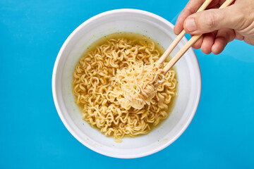 instant noodles eating using bamboo chopstick. caucasian male person eat fast food. flat lay. copy space. blue background.