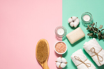 Spa and wellness concept. Brush for dry massage, Himalaya salt, natural soap, candles, towels and decor on two tone background top view. Skin care and home spa procedures.