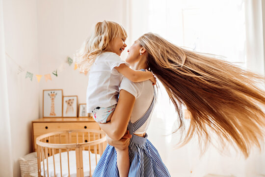 Young mother or babysitter with a little girl in her arms spin in the middle of the room
