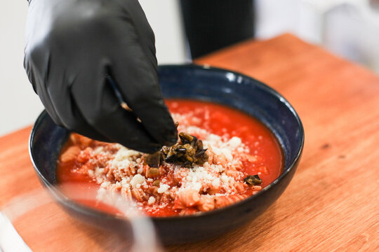 Close up picture of a cook's hand putting fresh parmesan cheese on a tomato pasta in a deep plate