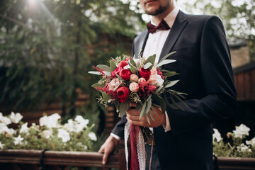 Beautiful bouquet in the hands of the man. Groom holding wedding, Bouquet of of red and pink buds of roses and peonies, eucalyptus branches in man's hands