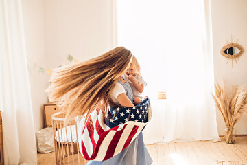 Young mother or babysitter with a little girl in her arms spin in the middle of the room celebrating July 4th Independence Day