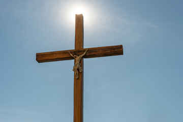 An old wooden Catholic cross against the background of the sun and clear blue sky. Religion and service to God as a path to redemption from sin. The face of Jesus crucified on the cross.