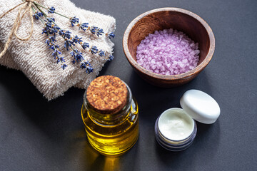 Fototapeta na wymiar Lavender blossom, sea salt, cream jar, towels and essential oil on black background, top view