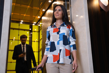 Businesswoman exiting a lift while her male colleague standing on behind