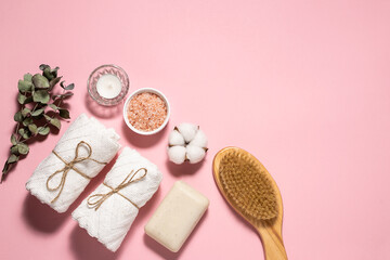 Skin care and home spa procedures concept with sea salt, brush for dry massage, towels, candles and natural soap on pink pastel background.