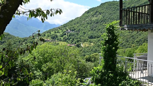 Beautiful view of the green mountains, plants on the left and the balconies of a house on the right frame the beautiful countryside in the background. Sunny day.