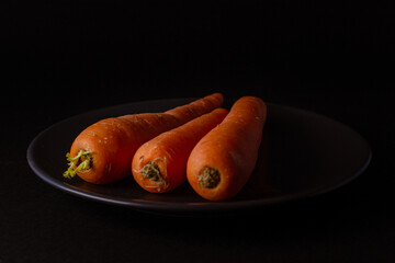 zanahorias frescas naturales en un plato negro sobre fondo negro