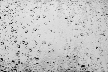 High contrast photo of drops of rain on a window glass with light gray color
