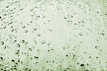 High contrast photo of drops of rain on a window glass with olive green color