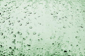 High contrast photo of drops of rain on a window glass with emerald green color