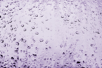 High contrast photo of drops of rain on a window glass with  light lilac color