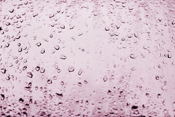 High contrast photo of drops of rain on a window glass with light red scarlet color