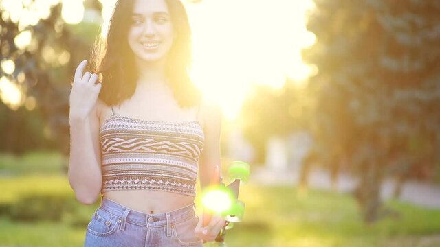 sport, lifestyle, Extreme and people concept - Beautiful girl on the road in the city in sunny weather. Portrait hipster girl smiling with a longboard at sunset. Slow motion