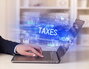 Closeup of businessman hands working on laptop with TAXES inscription, succesfull business concept