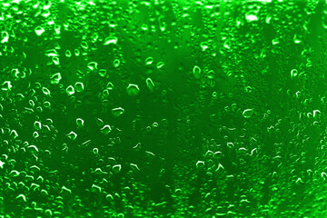 High contrast photo of drops of rain on a window glass with vivid emerald green color