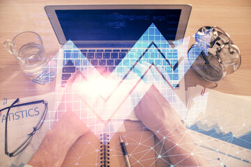Double exposure of man's hands typing over computer keyboard and growing arrows hologram drawing....