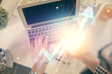 Double exposure of man's hands typing over computer keyboard and growing arrows hologram drawing. Top view. Success concept.