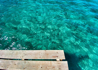 Wooden pier in the middle of transparent pristine turquoise sea water in Playa de Muro, Mallorca