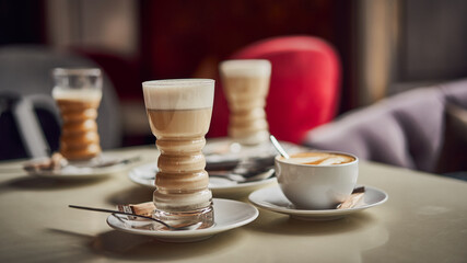 Latte glass with layered latte, cappuccino or mocha with foam on table in cafe with milk saucer and spoon. Three cups of coffee. Food and drink toning image. Web banner size 16 in 9 crop
