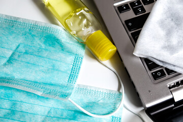 Virus prevention essentials: face masks, a yellow bottle of hand sanitizer and a napkin to clean a laptop. Home study or work environment during coronavirus outbreak isolation. Personal hygiene.