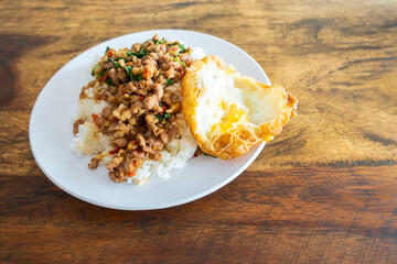 Rice topped with stir-fried pork and basil in  white dish on wooden table. , Text space.