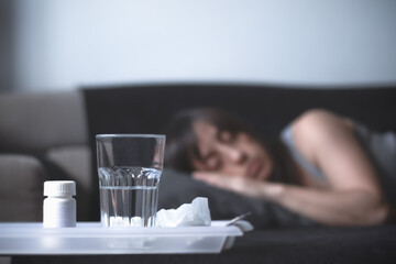 Mujer enferma dormida en el sofá con medicinas y vaso de agua