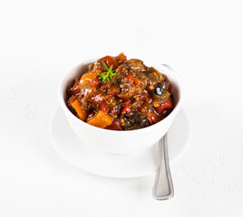 Vegetables baked in a bowl, zucchini, eggplant, tomatoes, carrots, onions with pepper and garlic on a light background