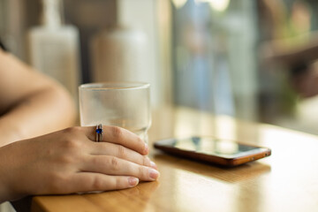 female hand in cafe table cozy picture with ring on fingers empty glass cup and unfocused phone on background
