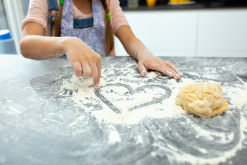 Little girl drawing heart shape with flour in kitchen
