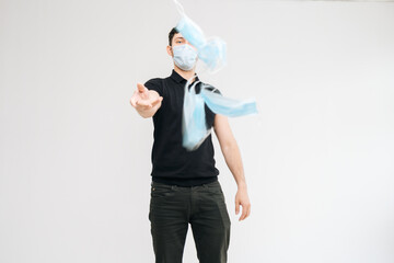 Portrait of young confident man wearing protective mask counting medical masks in his hand and throws them towards the cameras, on isolated white background. Prevention of virus infection.