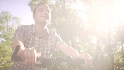 Middle age happy calm man in plaid shirt riding slow urban bicycle on empty street on summer sunny day in low angle shot