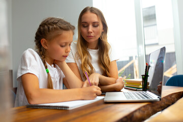 Loving mother helping daughter to study at home
