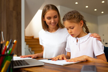Joyful young woman helping her daughter to study at home