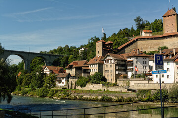 Fototapeta premium Beautiful scenery of Saane river, apartment buildings, the Red Tower and Saint Jean bridge in old town of Fribourg, Switzerland. Inscription translation: 