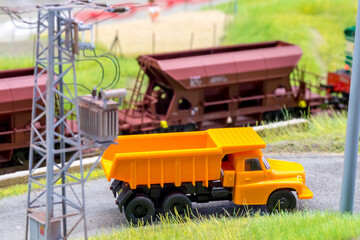 Orange truck on model train layout with moving freight train in behind