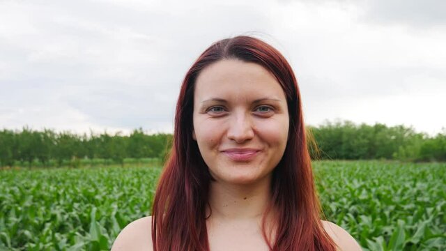 A portrait of a caucasian woman with red hair standing in a field smiling at the camera.