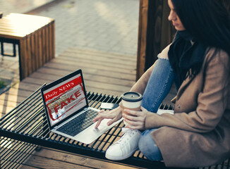 Happy woman with laptop in city center reading fake yellow news