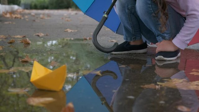 Wet paper boat. A little girl plays with a paper boat while sitting by a puddle under a multi-colored umbrella.