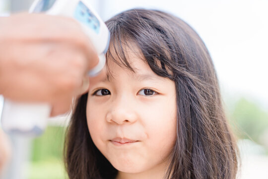 Temperature Check In School Kid Girl At School.Open School First Health Check Up Measurement.Asian Girl Measuring Body Temperature And Wearing A Face Mask Before Go Back To School.Healthcare Medical.