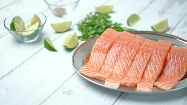 Close-up of slices of fresh raw red salmon.
Raw salmon in a silver plate on the wooden table with lemon and herbs/greens ingredients on the side. Concept of healthy seafood. Salmon 4K.