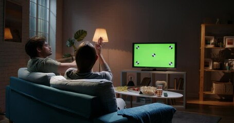 Emotional sports fan couple spending time together watching chroma-key green screen tv and reacting to their team play. 4k footage template - Powered by Adobe