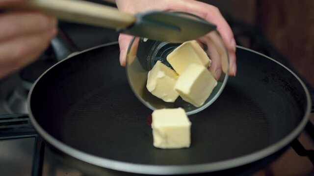 Placing butter cubes in a hot pan and melting them with a spatula. Concept of melting butter on a gas stove in 4k.