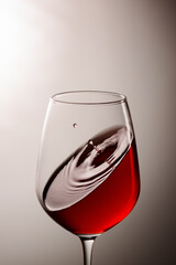 A glass of red wine with drops in the air.