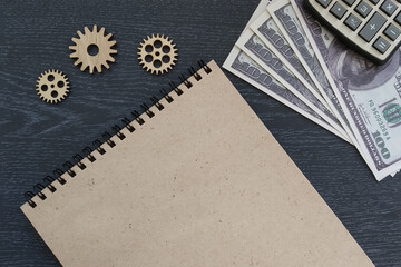 Notepad, wooden gears, American dollar bills, calculator on a dark background.Business planning, ideas.