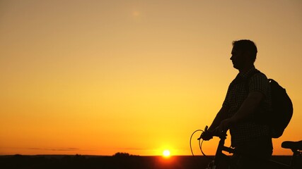 lonely cyclist resting in the park. healthy young man riding a bicycle along edge of hill, enjoying nature and sun. A free traveler travels with a bicycle at sunset. concept of adventure and travel.